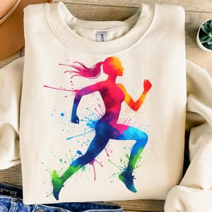 May include: A cream colored sweatshirt with a colorful watercolor silhouette of a person running. The silhouette is made up of shades of red, orange, yellow, green, blue, and purple.
