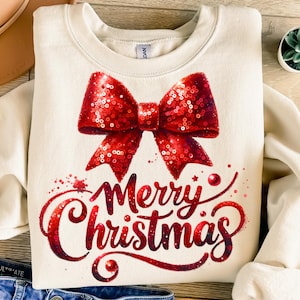 May include: Cream-colored sweatshirt featuring a large, sequined red bow and the words "Merry Christmas" in a festive script. The design includes red splatter accents, creating a holiday-themed graphic.