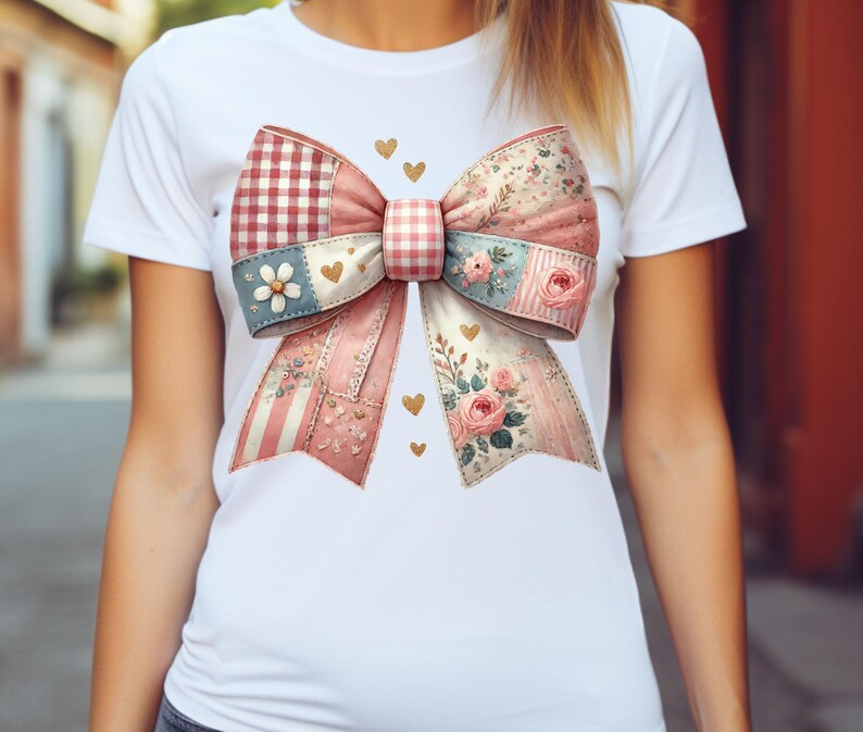 May include: White t-shirt featuring a large, decorative bow graphic. The bow is a patchwork design with pink, blue, and red patterns, including gingham, floral, and striped elements. Gold heart accents are scattered around the bow.