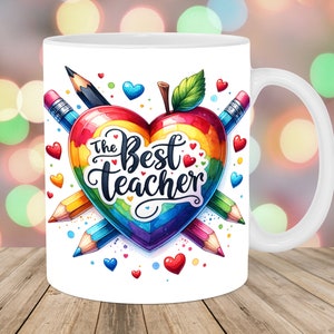 May include: White ceramic mug with a rainbow heart design and the text "The Best Teacher". The heart is made of pencils and has a red apple on top.