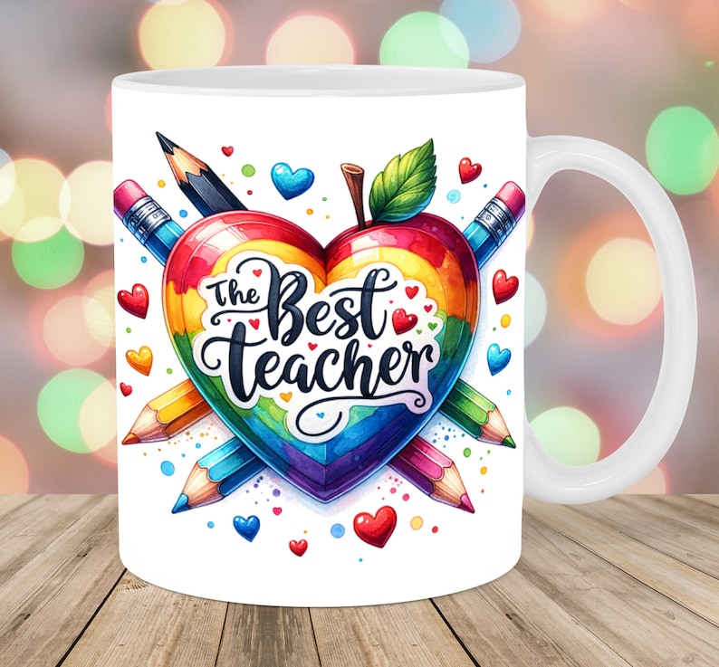 May include: White ceramic mug with a rainbow heart design and the text "The Best Teacher". The heart is made of pencils and has a red apple on top.