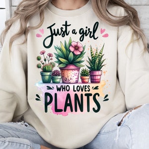 Może przedstawiać: Kremowa bluza z napisem "Just a girl who loves plants" w czarnym kolorze. Tekst jest otoczony r&oacute;żowymi sercami i akwarelowym wzorem doniczkowych roślin z zielonymi liśćmi i r&oacute;żowymi kwiatami.