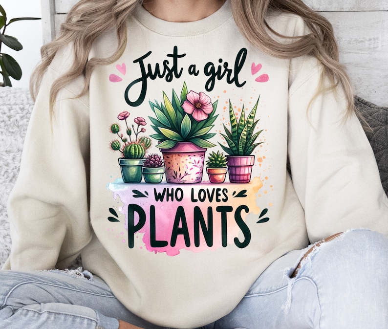 Może przedstawiać: Kremowa bluza z napisem "Just a girl who loves plants" w czarnym kolorze. Tekst jest otoczony r&oacute;żowymi sercami i akwarelowym wzorem doniczkowych roślin z zielonymi liśćmi i r&oacute;żowymi kwiatami.