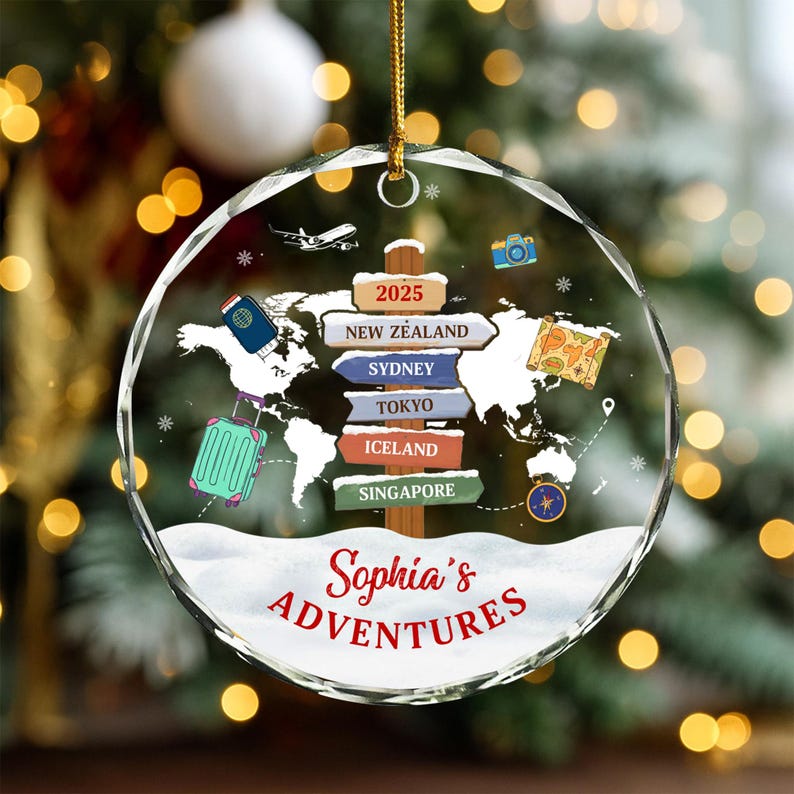 May include: A clear, round Christmas ornament with a world map design. The ornament features a signpost with destinations like New Zealand, Sydney, and Tokyo. It includes a suitcase, passport, camera, and the text "Sophia's Adventures" in red.