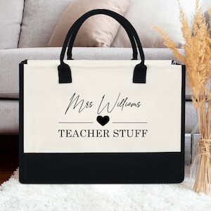 May include: A white canvas tote bag with black handles and a black bottom. The bag has the text "Mrs. Williams" in a cursive font with a heart symbol and the text "TEACHER STUFF" printed on it.