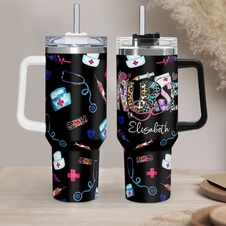 May include: Two black stainless steel travel mugs with a white handle and a black lid. The mugs are decorated with a colorful pattern of medical symbols, including a stethoscope, a syringe, a bandage, and a nurse's cap. The text "NURSE" is written in colorful letters on one mug, and the name "Elizabeth" is written on the other mug.