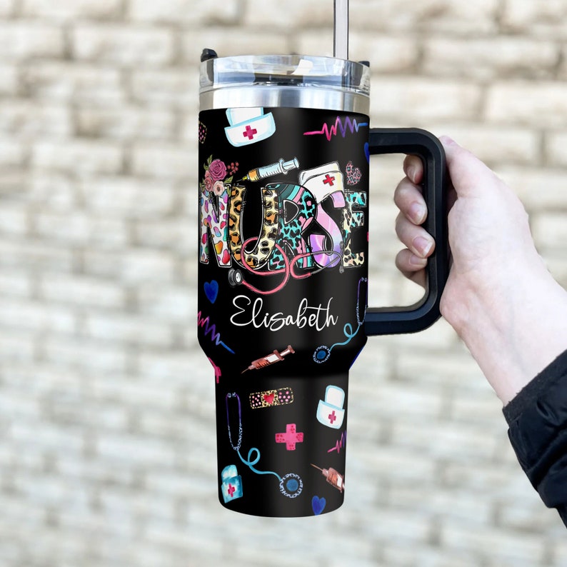 May include: A black stainless steel travel mug with a handle. The mug has a colorful design with the word "NURSE" and the name "Elizabeth". The design also includes medical symbols like a stethoscope, a syringe, and a bandage.