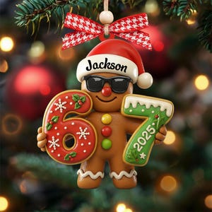 May include: A gingerbread man Christmas ornament wearing sunglasses and a Santa hat with the name "Jackson". The ornament holds the numbers "6" and "7" with the year "2025". The ornament is decorated with red, white, and green icing.