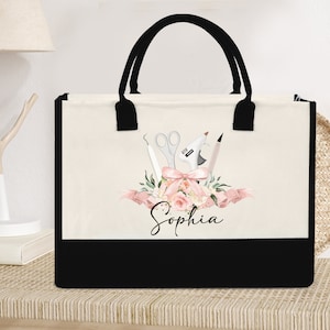 May include: A canvas tote bag with black handles and a black bottom panel. The bag features a floral design with craft tools, a pink bow, and the name "Sophia" in script.