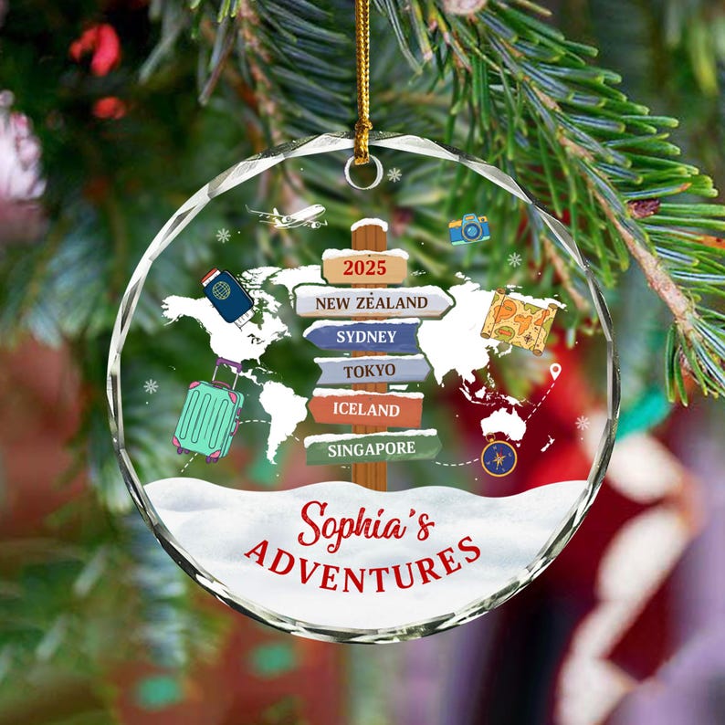 May include: A clear, round Christmas ornament with a world map design and the text "Sophia's Adventures." The ornament features a suitcase, passport, and destinations like New Zealand, Sydney, and Tokyo. A gold string is attached for hanging.