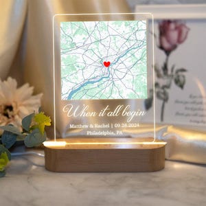 Op de afbeelding: Een helder acryl lichtbord met een kaart van Philadelphia, Pennsylvania. Het bord heeft een rood hart dat een locatie op de kaart markeert. De tekst op het bord luidt "When it all begin" en "Matthew & Rachel | 09.28.2024 Philadelphia, PA".