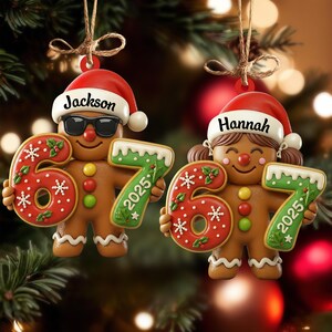 May include: Two gingerbread man Christmas ornaments. One wears sunglasses and has the name "Jackson" on its hat. The other has the name "Hannah" on its hat. Both hold the numbers "67" and "2025" in their hands. The ornaments are red, green, and brown.