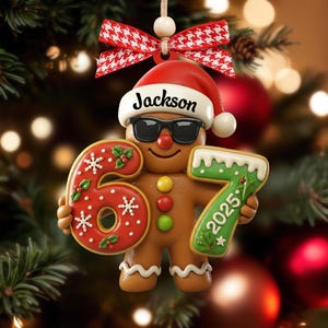 May include: A gingerbread man Christmas ornament wearing sunglasses and a Santa hat with the name "Jackson". The ornament holds the numbers "6" and "7" with the year "2025". The ornament is decorated with red, white, and green icing and is hanging from a red and white bow.