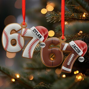 May include: Christmas tree decorations shaped as the numbers 6 and 7, styled as a baseball and a football. Each number has a Santa hat with a name and the year 2025. Red ribbons are attached for hanging.