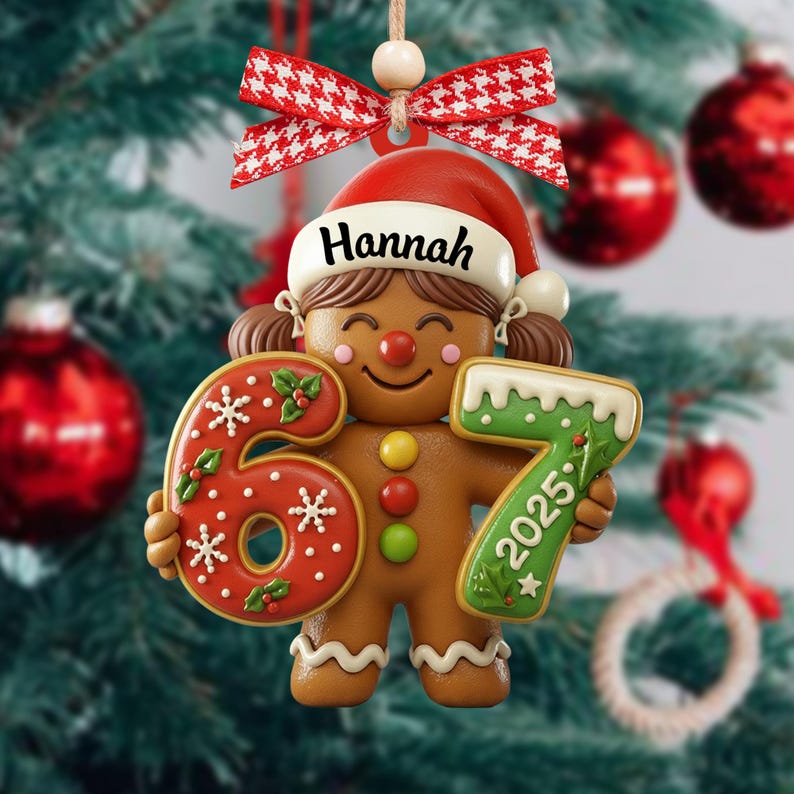 May include: A gingerbread-style Christmas ornament featuring a smiling girl wearing a Santa hat with the name "Hannah". The ornament holds the numbers "6" and "7" with "2025" on the "7". It is decorated with red and white accents.