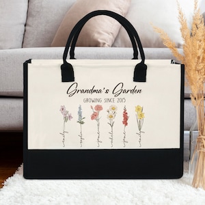 May include: A white canvas tote bag with black handles and a black bottom. The bag has a floral design with the text "Grandma's Garden Growing Since 2015" and the names of family members.