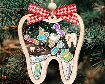 May include: A wooden tooth-shaped Christmas ornament with a red and white bow. The ornament is decorated with various dental tools and the text "Jessica Nurse" and "2024".