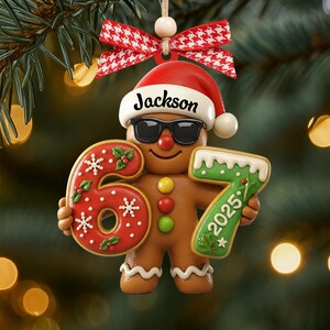 May include: A gingerbread man Christmas ornament wearing sunglasses and a Santa hat with the name "Jackson". The ornament holds the numbers "6" and "7" with the year "2025". It is decorated with red, white, and green icing and a red and white checkered bow.