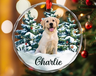May include: A clear, round Christmas ornament with a smiling yellow Labrador Retriever puppy inside. The ornament features a snowy scene with Christmas trees and the name "Charlie" in cursive. A red ribbon is attached for hanging.