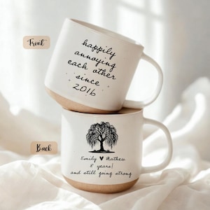 Puede incluir: Dos tazas de cerámica blanca apiladas. La taza superior tiene el texto "happily annoying each other since 2016". La taza inferior tiene un gráfico de árbol y el texto "Emily & Mathew 8 years! and still going strong".