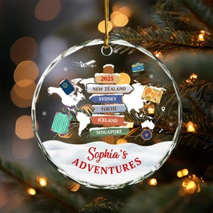 May include: A clear, round Christmas ornament with a world map design and travel-themed elements. Features a signpost with destinations like New Zealand, Sydney, and Tokyo. Includes a suitcase, passport, and the text "Sophia's Adventures".
