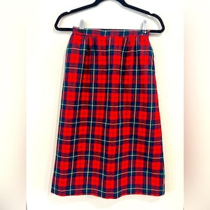 May include: A red plaid skirt with a black hanger. The skirt features a classic tartan pattern in red, navy blue, and green. The skirt is hanging against a white background.