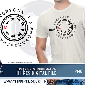 May include: A white t-shirt with a black graphic design of a camera aperture setting with the text "Everyone is a photographer until..." printed on the front.
