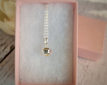 May include: A silver necklace with a delicate flower pendant. The flower is made of silver and has a textured surface. The necklace is in a pink box.