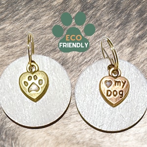 May include: Two round, white, dog tag charms with gold-colored metal rings. The charm on the left has a gold heart with a paw print inside. The charm on the right has a gold heart with the words "I love my dog" inside.