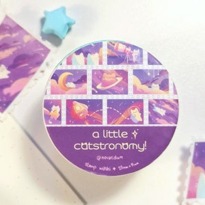 Pu&ograve; includere: Un rotolo di nastro washi viola e blu con un motivo ripetuto di gatti nello spazio. Il nastro &egrave; etichettato "a little catstronomy!" e "@novaridium stamp washi + 25mm x 8mm".