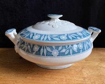 Puede incluir: Fuente de cerámica blanca y azul con tapa. La fuente presenta un patrón floral y de hojas en tonos azules. Las asas y el pomo de la tapa son blancos. La fuente está sobre una superficie de madera.