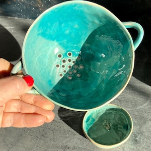 Può includere: Una tazza di ceramica bianca con manico nero e la scritta "But First, Coffee" in grassetto nero. La tazza è esposta su una superficie bianca. La tazza è alta circa 10 cm.