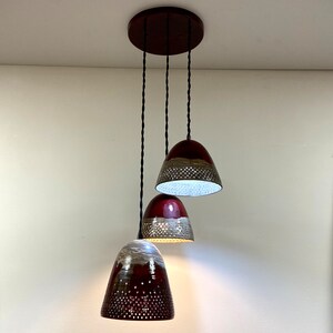May include: Three hanging pendant lights with a dark red and brown ceramic shade. Each shade has a pattern of small holes and a light brown band around the middle.