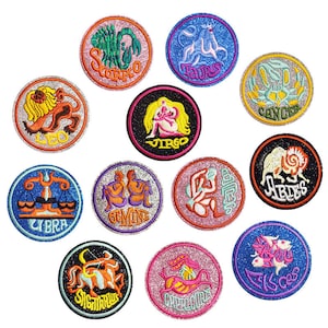 May include: A set of twelve circular embroidered patches, each representing a different zodiac sign. The patches have glittery backgrounds in various colours, with detailed illustrations and the sign's name in a contrasting colour. The signs include Aries, Taurus, Gemini, Cancer, Leo, Virgo, Libra, Scorpio, Sagittarius, Capricorn, Aquarius, and Pisces.