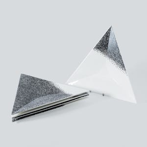 May include: Three white, triangular plates with a black speckled pattern on one corner. The plates are stacked and arranged on a white surface, creating a modern, minimalist look. The plates are made of ceramic.