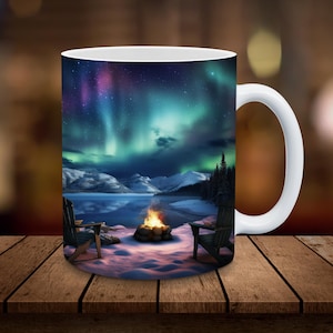 May include: White ceramic mug with a colorful aurora borealis scene. The mug features two chairs and a campfire in the foreground, with a lake and mountains in the background.