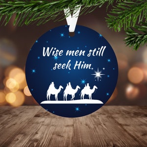 May include: A blue round Christmas ornament with a white silhouette of three wise men riding camels. The ornament has white stars and the text "Wise men still seek Him."