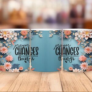 K&ouml;nnte beinhalten: Drei wei&szlig;e Keramikbecher mit blauem Hintergrund und floralem Design. Die Becher haben den Text "prayer changes things" in schwarzer Schrift.
