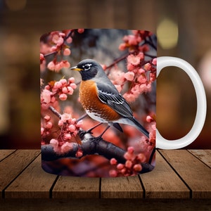 May include: A white ceramic mug with a colorful image of a robin perched on a branch with pink blossoms. The robin has a gray head, a black eye, an orange breast, and a long tail.