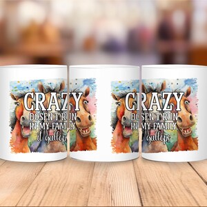 May include: White ceramic mug featuring a watercolor illustration of three horses with the text "CRAZY DOESN'T RUN IN MY FAMILY it gallops". The horses are in shades of brown, orange, and blue.