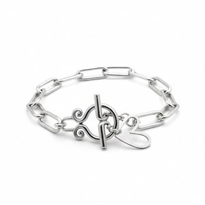 May include: A silver-colored bracelet with a chain link design. The bracelet features a decorative clasp with a heart-shaped element. The links are rectangular and the clasp has a toggle closure.