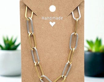 May include: A handmade necklace with a chain link design. The necklace features alternating gold and silver-colored links. The necklace is displayed on a brown card with the word "Handmade" and a heart symbol.
