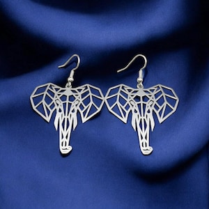 May include: A pair of silver geometric elephant earrings. The earrings are made of metal and have a geometric design. The earrings are hanging from silver hooks.