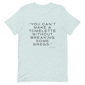 Pode incluir: Uma camiseta azul clara com uma citação em texto preto que diz "You can't make a tomette without breaking some Gregs." A citação é atribuída a Gil Eavis.