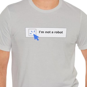 May include: Light gray t-shirt with a graphic that says "I'm not a robot." The graphic includes a blue cursor and a small box with a checkmark inside. The shirt is short-sleeved and has a crew neck.