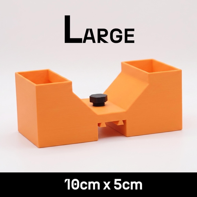 May include: An orange plastic tool with two rectangular openings and a central black knob. The text LARGE is printed above the object, and the text 10cm x 5cm is printed below. The object features a bridge-like structure with a hollow center.