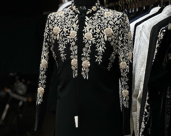 May include: A black formal jacket with detailed gold floral embroidery. The jacket has a mandarin collar and long sleeves, with the floral design cascading down the front and sleeves. The garment is displayed on a mannequin.
