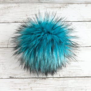 May include: A fluffy teal and black faux fur pom pom. The pom pom is made of soft, synthetic fur and is perfect for adding a touch of whimsy to any hat or accessory.