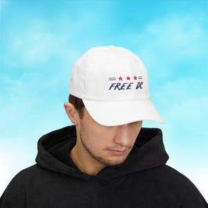May include: White baseball cap with the text "FREE DC" in navy blue, with red stars and navy blue horizontal lines. The cap is made of a soft material and has a curved brim. The cap is a casual accessory.