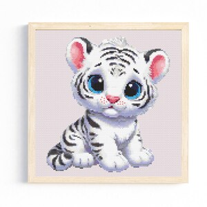 Könnte beinhalten: Ein weißer Tigerwelpe mit blauen Augen und rosa Ohren sitzt auf einem hellvioletten Hintergrund. Der Tiger hat schwarze Streifen und eine weiße Nase.